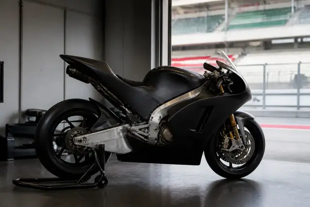 Moto de Grand Prix de profil dans un garage de circuit, carénage aérodynamique et pneus slicks, sans marque ni numéro lisible
