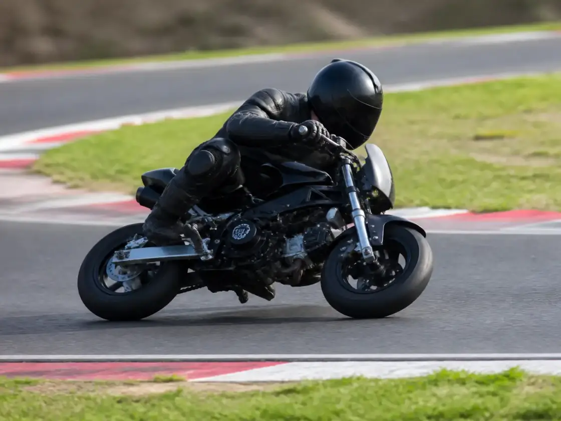 Adulte casqué sur une petite moto de piste, dans un virage serré d’un tracé de loisir, vue de profil, aucun lieu reconnaissable
