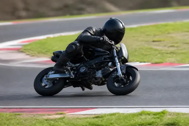 Adulte casqué sur une petite moto de piste, dans un virage serré d’un tracé de loisir, vue de profil, aucun lieu reconnaissable