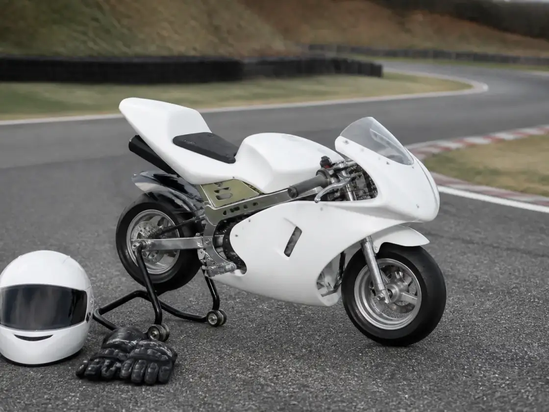 Moto pocket de très petit gabarit posée sur un support de paddock, à côté d’une paire de gants et d’un casque de piste