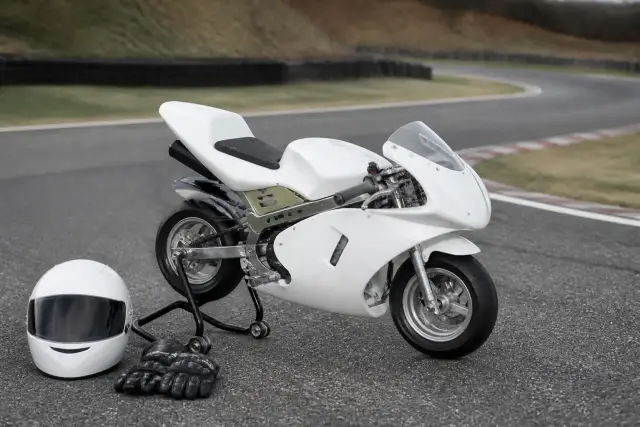 Moto pocket de très petit gabarit posée sur un support de paddock, à côté d’une paire de gants et d’un casque de piste