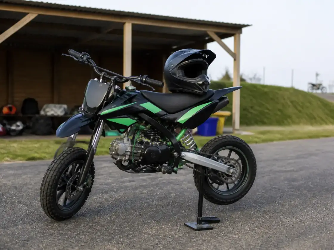 Petite moto de type pit bike garée dans un paddock de piste de loisir, casque posé sur la selle, aucun lieu ni inscription reconnaissable