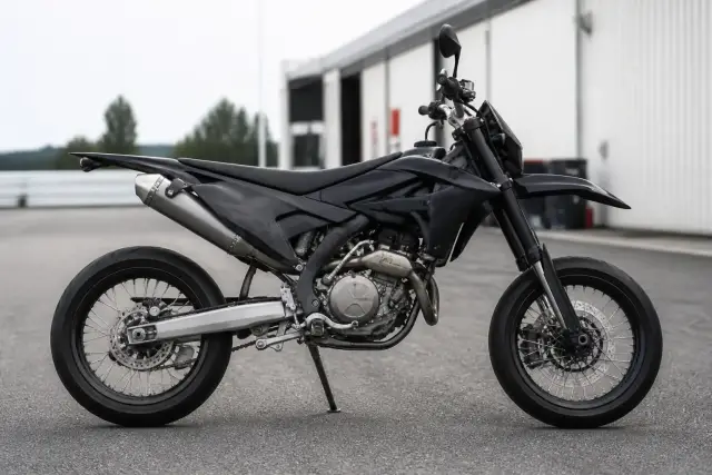 Moto de type supermotard avec grandes roues de route et suspension haute, vue de profil sur une aire de paddock goudronnée