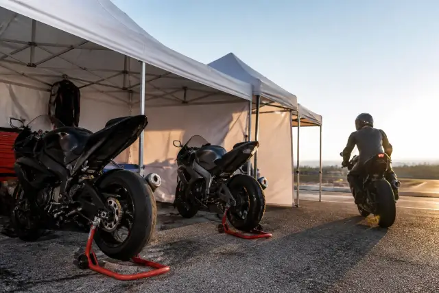 Vue large d’un paddock avec des motos sur béquille d’atelier, des tentes blanches et un ciel clair de début de journée