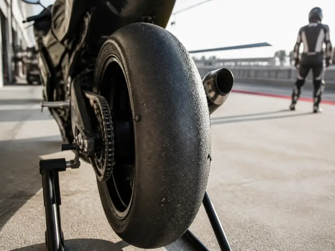 Pneu arrière d’une moto de circuit en gros plan, bande de roulement lisse sur le centre et gommée sur les bords, roue posée sur un support d’atelier