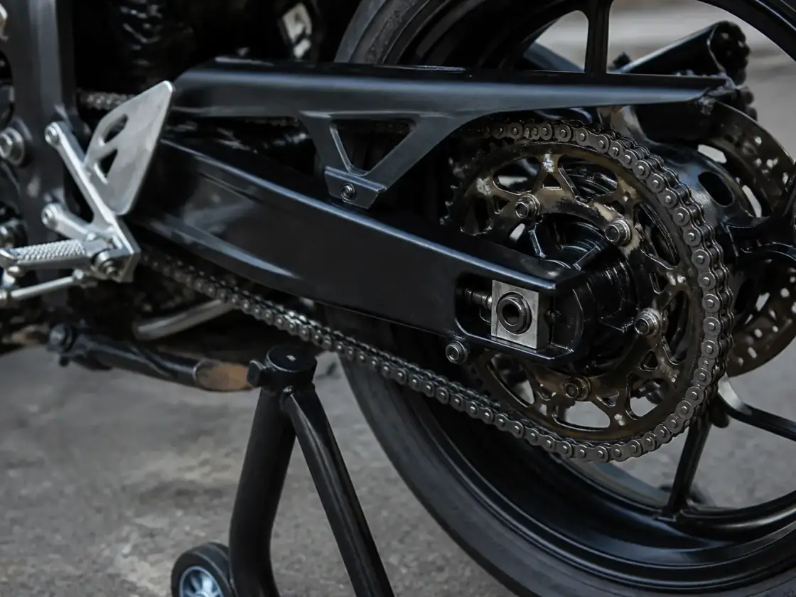Chaîne de transmission d’une moto de circuit et couronne arrière, vues de près, roue arrière légèrement soulevée sur béquille d’atelier