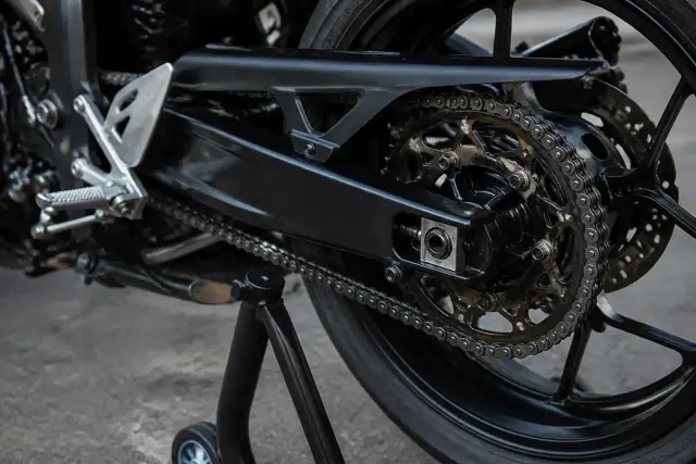 Chaîne de transmission d’une moto de circuit et couronne arrière, vues de près, roue arrière légèrement soulevée sur béquille d’atelier
