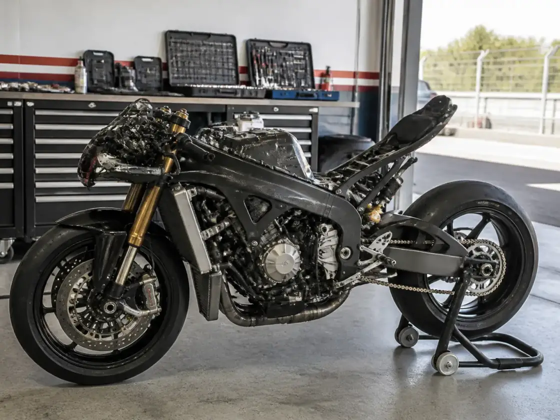 Moto de circuit sur béquille dans un box de paddock, carénages déposés pour un contrôle, outils rangés sur un établi voisin