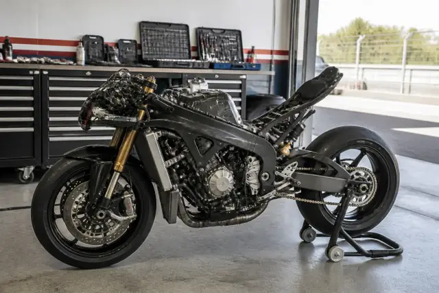 Moto de circuit sur béquille dans un box de paddock, carénages déposés pour un contrôle, outils rangés sur un établi voisin