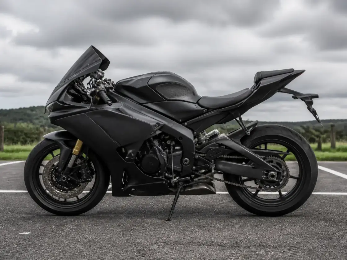 Moto sportive carénée de profil, à l’arrêt sur un parking d’asphalte, sans marque ni plaque lisible, ciel nuageux