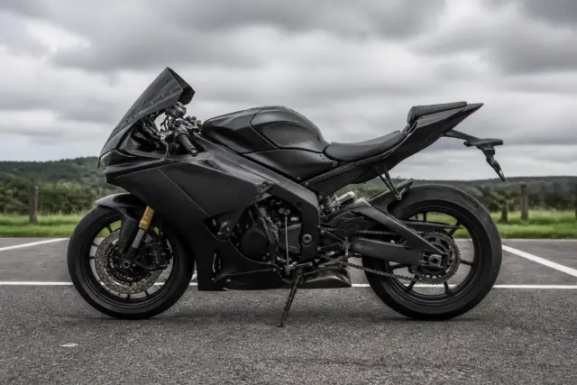 Moto sportive carénée de profil, à l’arrêt sur un parking d’asphalte, sans marque ni plaque lisible, ciel nuageux