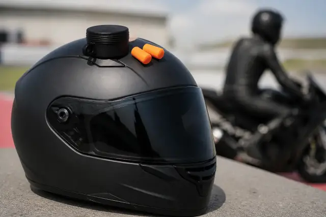 Deux bouchons d’oreille en mousse et un étui posés sur un casque de moto intégral, fond gris neutre