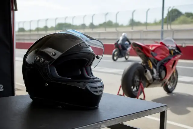 Casque intégral de course posé sur une table de stand, visière relevée, jugulaire apparente, sans marque lisible