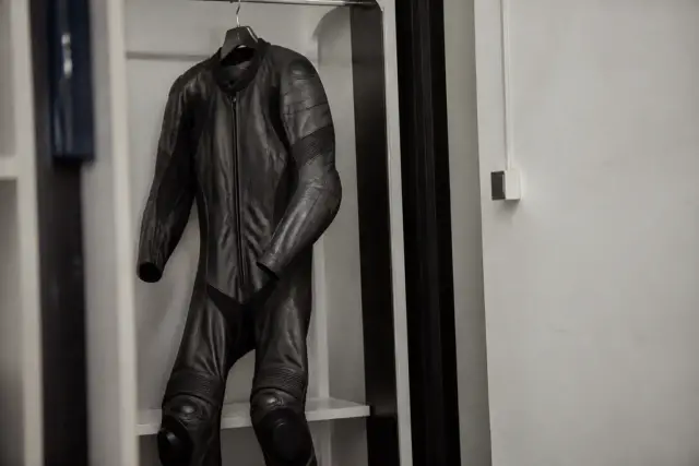 Combinaison de cuir de moto sombre, pendue à un cintre dans un vestiaire neutre, coudes et genoux renforcés visibles