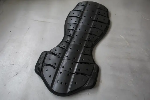 Dorsale de moto posée à plat sur une table de travail grise, plaques articulées noires, sans marque visible