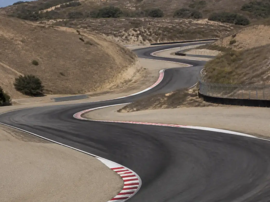 Vue plongeante sur un enchaînement de virages en descente d’un circuit de moto californien, vibreurs et gravier en bord de piste, aucun pilote identifiable