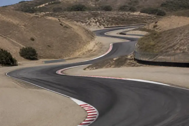 Vue plongeante sur un enchaînement de virages en descente d’un circuit de moto californien, vibreurs et gravier en bord de piste, aucun pilote identifiable