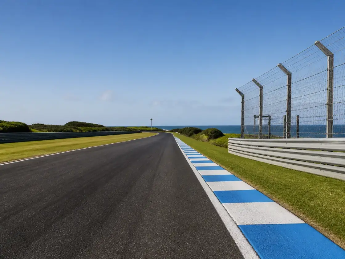 Piste de course sur une île australienne, ligne droite bordée de vibreurs et de clôtures, herbe rase et ciel dégagé, aucune moto ni numéro lisible