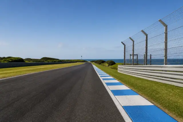 Piste de course sur une île australienne, ligne droite bordée de vibreurs et de clôtures, herbe rase et ciel dégagé, aucune moto ni numéro lisible