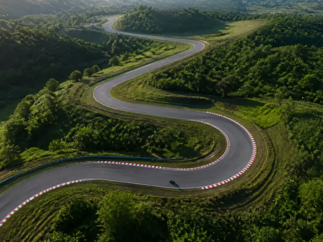 Vue aérienne d’un tracé de circuit sinueux entre des collines vertes, ruban de bitume bordé de vibreurs rayés rouge et blanc, lumière du matin