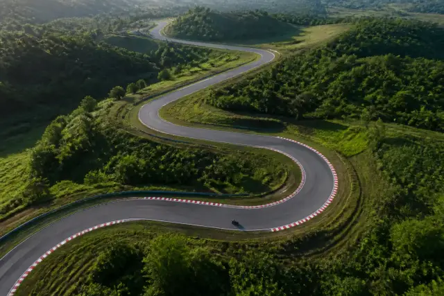 Vue aérienne d’un tracé de circuit sinueux entre des collines vertes, ruban de bitume bordé de vibreurs rayés rouge et blanc, lumière du matin