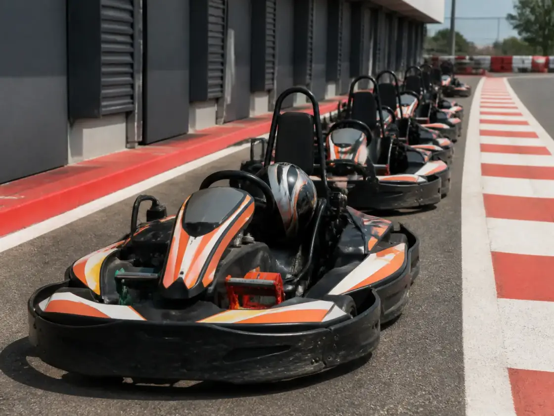 Karts de loisir alignés dans la voie des stands d’une piste de karting, casques posés sur les sièges, vibreur rouge et blanc