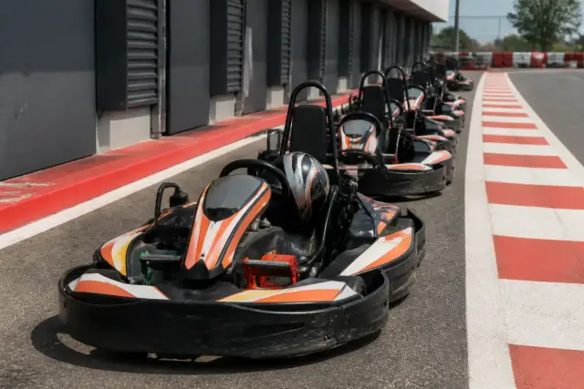 Karts de loisir alignés dans la voie des stands d’une piste de karting, casques posés sur les sièges, vibreur rouge et blanc